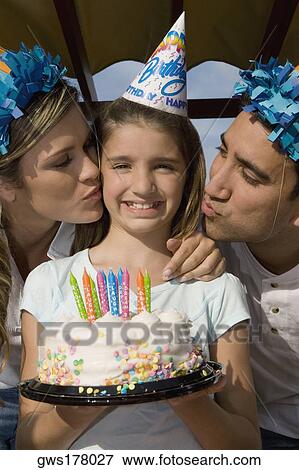 Stock Photo - Portrait of a girl holding a birthday cake and her parents kissing her. Fotosearch