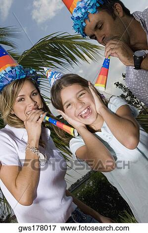 Portrait of a girl laughing with her parents blowing party horn blowers View Large Photo Image Stock Photo - Portrait of a girl laughing with her parents blowing party horn blowers. Fotosearch