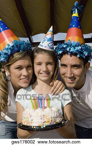 Stock Image - Portrait of a girl with her parents holding a birthday cake and smiling. Fotosearch