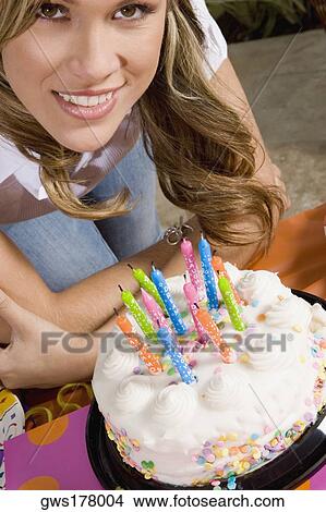Portrait of a young woman standing in front of a birthday cake and smiling View Large Photo Image Picture - Portrait of a young woman standing in front of a birthday cake and smiling. Fotosearch
