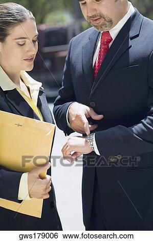 Businessman and a businesswoman checking the time in a wristwatch View Large Photo Image Stock Photograph - Businessman and a businesswoman checking the time in a wristwatch. Fotosearch