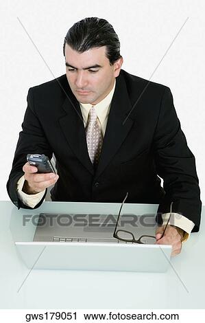 Stock Image - Businessman using a mobile phone in front of a laptop. Fotosearch