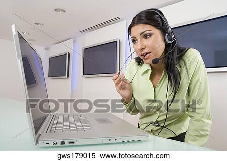 Close-up of a young woman wearing a headset and looking at a laptop View Large Photo Image Stock Photography - Close-up of a young woman wearing a headset and looking at a laptop. Fotosearch