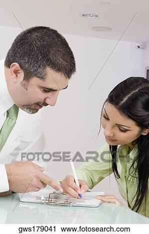 Stock Image - Receptionist writing on a clipboard with a businessman talking to her. Fotosearch