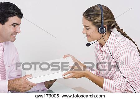 Stock Photography - Side profile of a receptionist wearing a headset and receiving a box from a businessman. Fotosearch