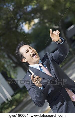 Businessman holding a mobile phone and shouting View Large Photo Image Picture - Businessman holding a mobile phone and shouting. Fotosearch