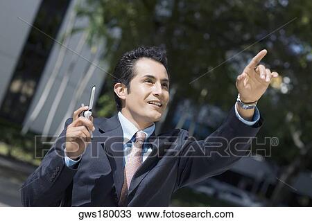 Businessman holding a mobile phone and pointing upward View Large Photo Image Stock Image - Businessman holding a mobile phone and pointing upward. Fotosearch