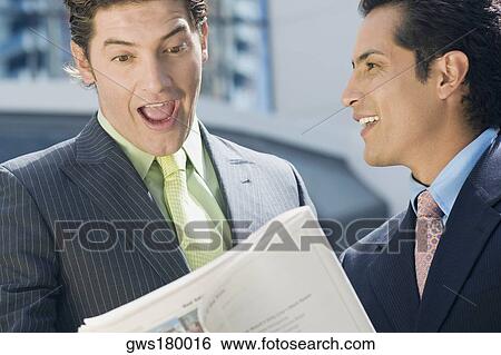 Businessman looking at a stock exchange report with another businessman standing beside him and smiling View Large Photo Image Stock Photograph - Businessman looking at a stock exchange report with another businessman standing beside him and smiling. Fotosearch