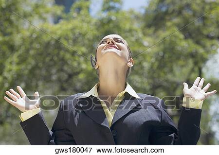 Stock Photo - Businesswoman looking up with her arms raised. Fotosearch