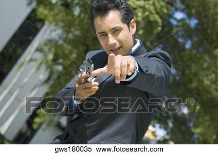 Stock Photography - Portrait of a businessman holding a mobile phone and pointing forward. Fotosearch