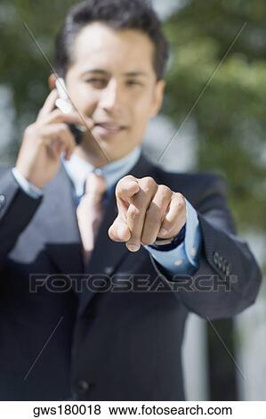 Stock Photo - Portrait of a businessman talking on a mobile phone and pointing forward. Fotosearch