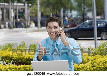 Stock Photography - Portrait of a businessman talking on a mobile phone and showing a thumbs up sign. Fotosearch
