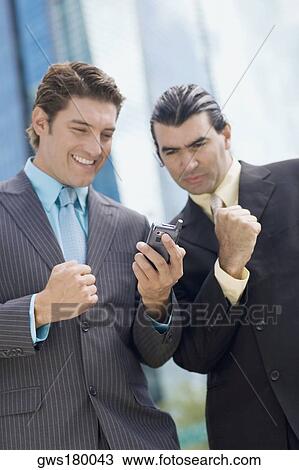 Stock Image - Two businessmen looking at a hand held device. Fotosearch