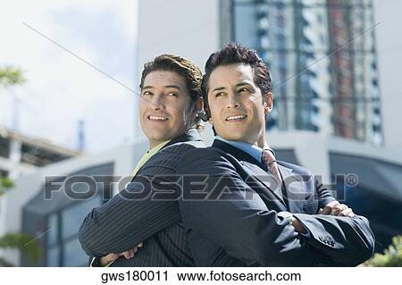 Stock Image - Two businessmen standing back to back and smiling. Fotosearch