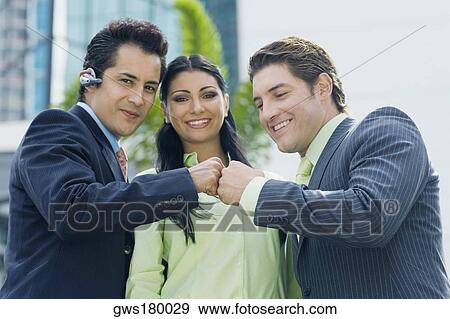 Two businessmen touching knuckles and a businesswoman smiling View Large Photo Image Stock Photo - Two businessmen touching knuckles and a businesswoman smiling. Fotosearch