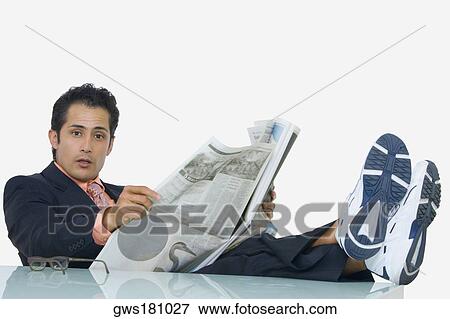 Stock Photo - Portrait of a businessman resting his legs on the table and reading a newspaper. Fotosearch