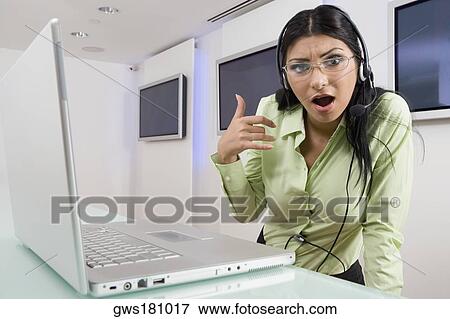 Stock Photo - Portrait of a young woman wearing a headset and standing in front of a laptop. Fotosearch
