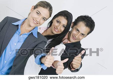 Stock Image - Portrait of two businesswomen and a businessman standing in a row and making a thumbs up sign. Fotosearch