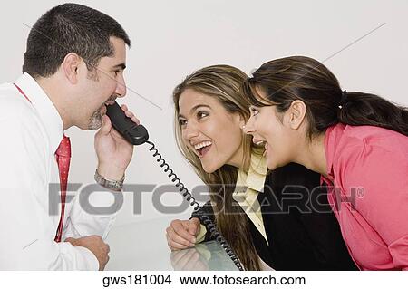 Side profile of a businessman talking on the telephone with two businesswomen looking at him and smiling View Large Photo Image Picture - Side profile of a businessman talking on the telephone with two businesswomen looking at him and smiling. Fotosearch