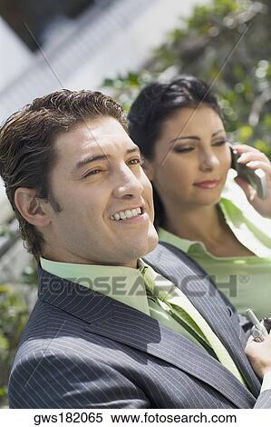 Stock Photography - Close-up of a businessman smiling with a businesswoman talking on a mobile phone. Fotosearch