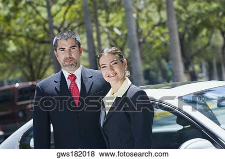 Stock Photo - Portrait of a businesswoman standing with a businessman in front of a car. Fotosearch