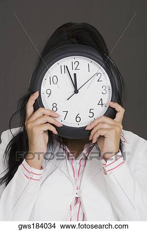 Picture - Close-up of a businesswoman holding a clock in front of her face. Fotosearch