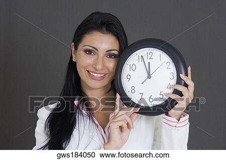 Close-up of a businesswoman holding a clock and smiling View Large Photo Image Stock Image - Close-up of a businesswoman holding a clock and smiling. Fotosearch