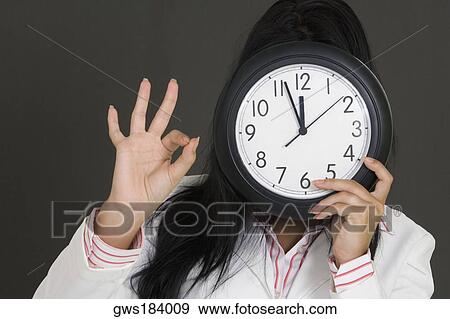 Close-up of a businesswoman holding a clock in front of her face and making an OK sign View Large Photo Image Stock Photo - Close-up of a businesswoman holding a clock in front of her face and making an OK sign. Fotosearch
