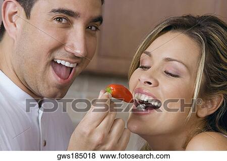 Stock Photo - Close-up of a mid adult man feeding a red chili pepper to a young woman. Fotosearch