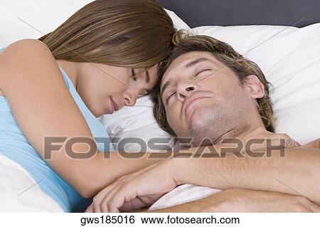 Stock Photograph - Close-up of a mid adult man sleeping on the bed with a young woman. Fotosearch