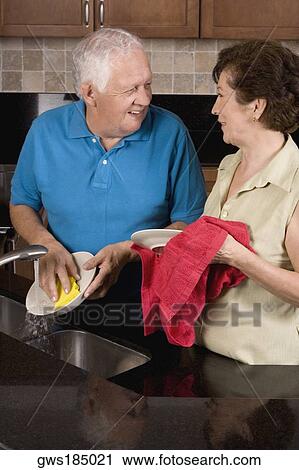 Stock Image - Close-up of a senior couple cleaning plates in the kitchen. Fotosearch