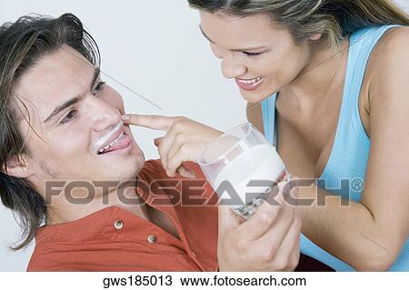 Stock Image - Close-up of a young woman touching milk mustache of a young man and smiling. Fotosearch