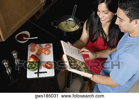 Stock Image - High angle view of a couple preparing food with the help of a cookbook in the kitchen. Fotosearch