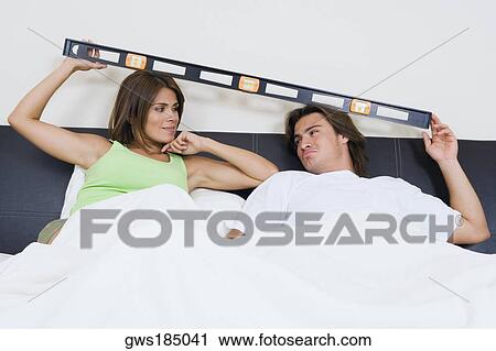 Stock Image - Young couple reclining on the bed with a spirit level over their heads. Fotosearch