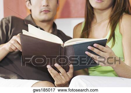 Young couple sitting on a couch and holding a book View Large Photo Image Stock Photo - Young couple sitting on a couch and holding a book. Fotosearch
