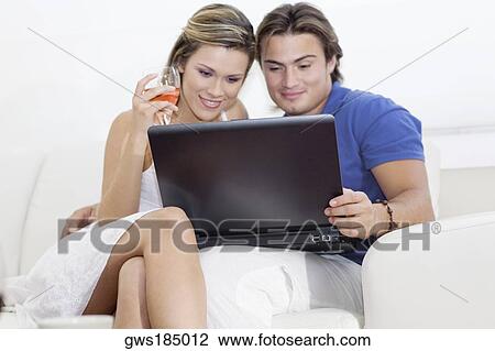 Young man looking at a laptop with a young woman holding a wine glass and sitting beside him View Large Photo Image Stock Image - Young man looking at a laptop with a young woman holding a wine glass and sitting beside him. Fotosearch