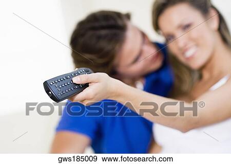 Young woman holding a remote control with a young man kissing her View Large Photo Image Stock Photo - Young woman holding a remote control with a young man kissing her. Fotosearch