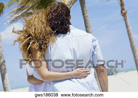 Mid adult couple walking on the beach with their arms around each other View Large Photo Image Stock Photo - Mid adult couple walking on the beach with their arms around each other. Fotosearch