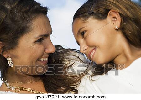 Close-up of a mid adult woman and her daughter looking at each other and smiling View Large Photo Image Stock Image - Close-up of a mid adult woman and her daughter looking at each other and smiling. Fotosearch