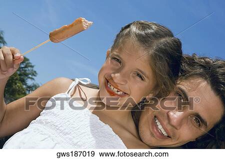 Stock Photo - Low angle view of a girl holding a sausage with her father. Fotosearch