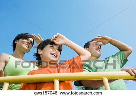 Low angle view of a mid adult couple standing with their son and shielding their eyes View Large Photo Image Stock Photograph - Low angle view of a mid adult couple standing with their son and shielding their eyes. Fotosearch