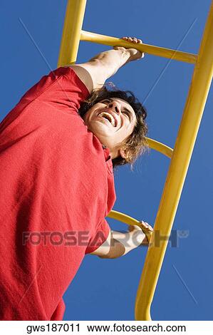 Stock Image - Low angle view of a mid adult man hanging on monkey bars. Fotosearch