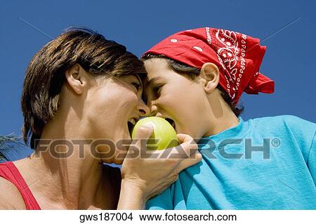 Low angle view of a mid adult woman biting an apple with her son View Large Photo Image Picture - Low angle view of a mid adult woman biting an apple with her son. Fotosearch