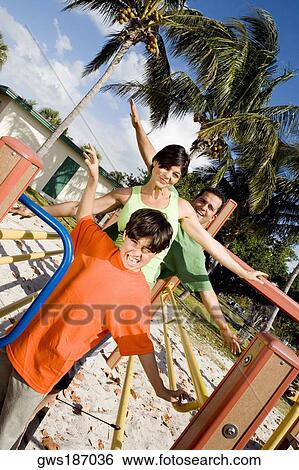 Mid adult couple standing on a jungle gym with their son and smiling View Large Photo Image Stock Photograph - Mid adult couple standing on a jungle gym with their son and smiling. Fotosearch