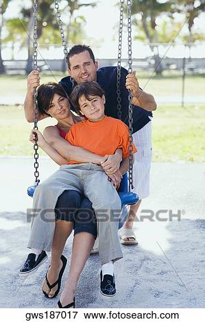 Stock Photo - Mid adult woman sitting on a swing with her son and a mid adult man pushing them. Fotosearch