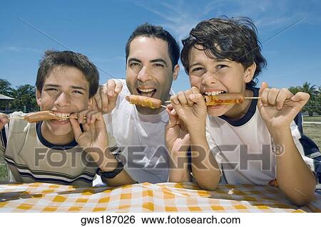 Portrait of a mid adult man with his two sons eating sausages in a picnic View Large Photo Image Stock Photograph - Portrait of a mid adult man with his two sons eating sausages in a picnic. Fotosearch