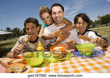 Two boys eating sausages with their parents in a picnic View Large Photo Image Stock Image - Two boys eating sausages with their parents in a picnic. Fotosearch