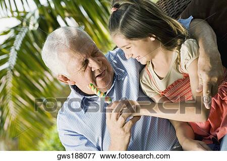 Stock Photo - Girl sitting with her grandfather and holding a candy. Fotosearch