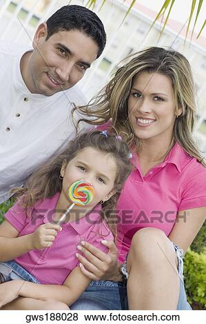 Portrait of a girl holding a lollipop with her parents in a park View Large Photo Image Stock Photo - Portrait of a girl holding a lollipop with her parents in a park. Fotosearch