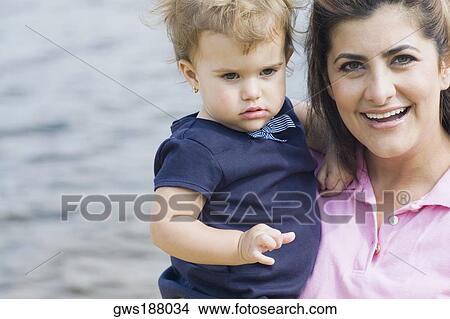 Picture - Portrait of a mid adult woman carrying her son and smiling. Fotosearch